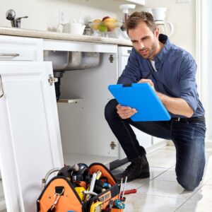 Plumber kneeling and writing near a broken sink