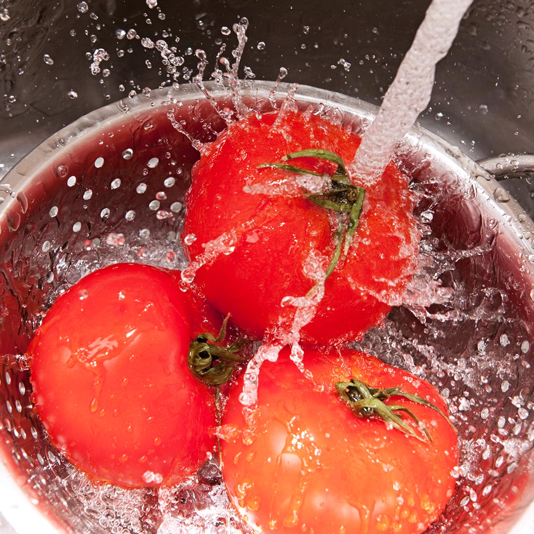 tomatoes being rinsed in a strainer in the sink