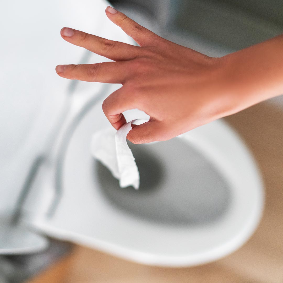hand holding a piece of toilet paper over a toilet